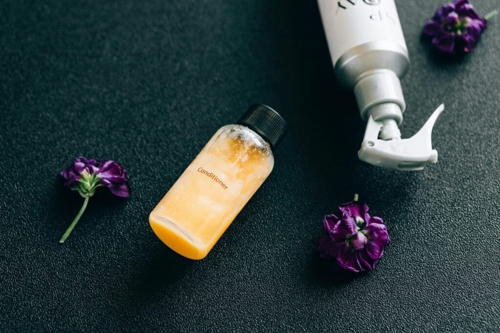 Elegant flat lay of conditioner and spray bottle with vibrant purple flowers on dark background.